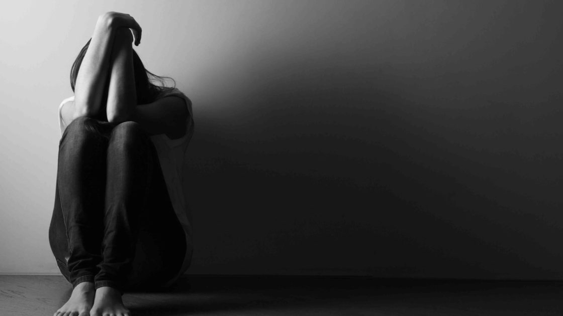 teen girl sitting alone on the floor in a dark room